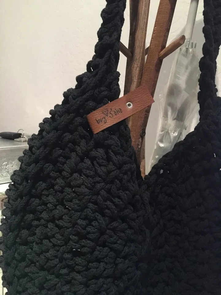 El bolso en negro, con su tira grabada, colgado de un perchero