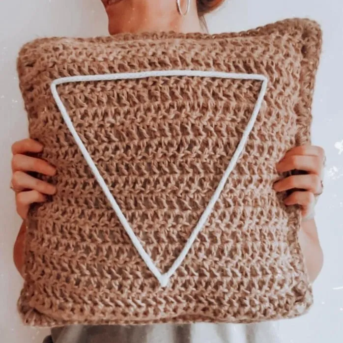 Cojín de crochet en camel con el triángulo de BY S’OHO en cordón blanco, sostenido con las dos manos