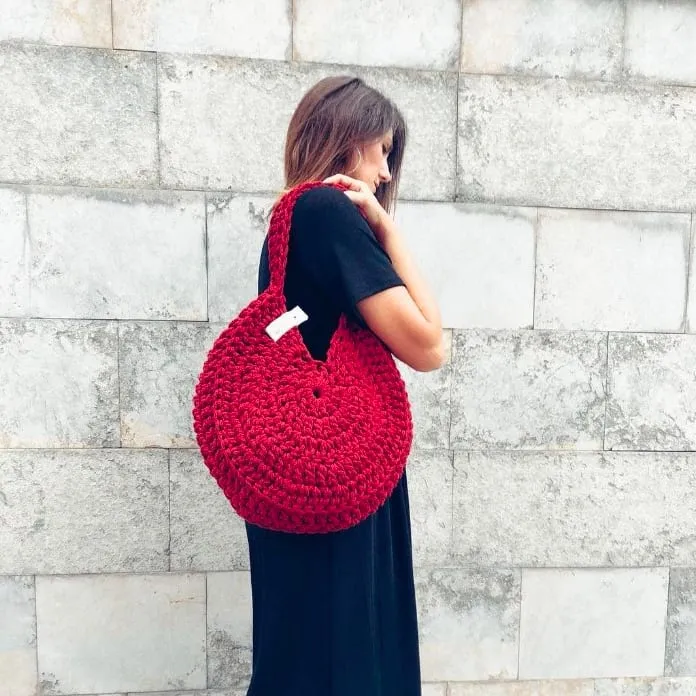 Una clienta con el bolso de crochet en rojo al hombro, delante de un muro de piedra